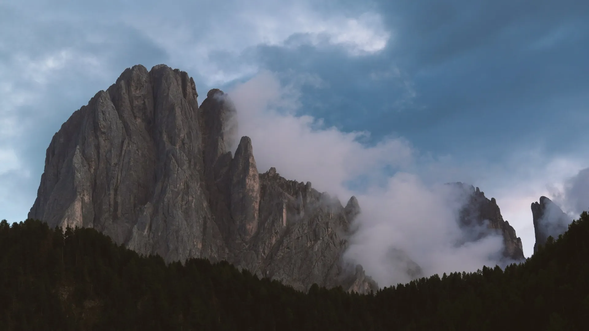 An athlete hikes across a dramatic alpine ridgeline beneath a mountain sky.