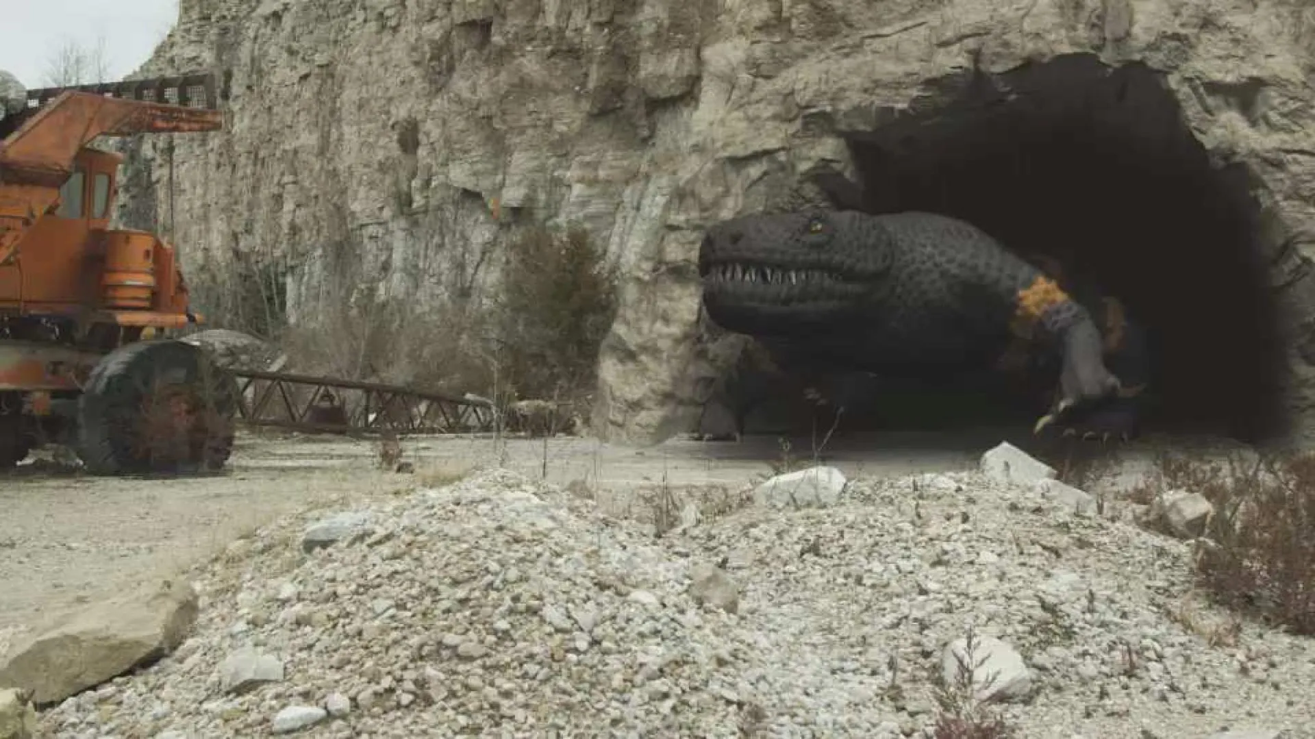 A giant Gila monster emerges from a rocky cave in a production still.